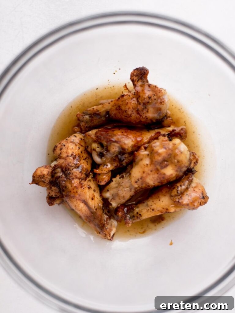 Baked chicken wings in a mixing bowl with the tequila lime glaze poured over them, ready to be tossed.