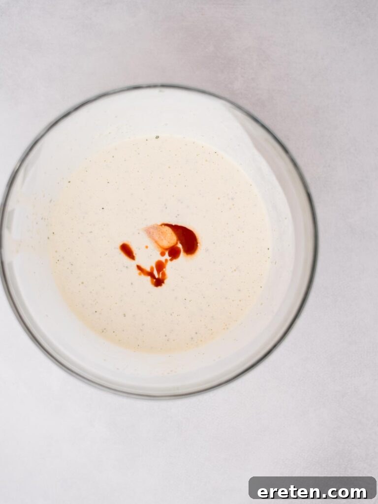 Bold Ranch Kick 6 Buffalo sauce being drizzled into the mixed ranch dressing base.