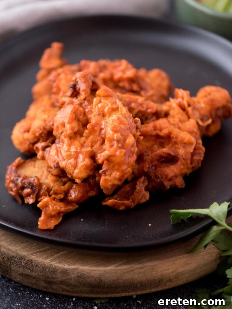 Crispy boneless wings coated in fiery buffalo sauce, garnished with fresh parsley on a sleek black plate.