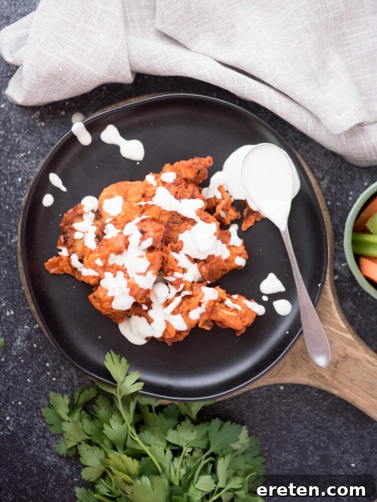 Boneless wings artfully drizzled with creamy ranch dressing and garnished with fresh parsley, presented on a chic black plate.