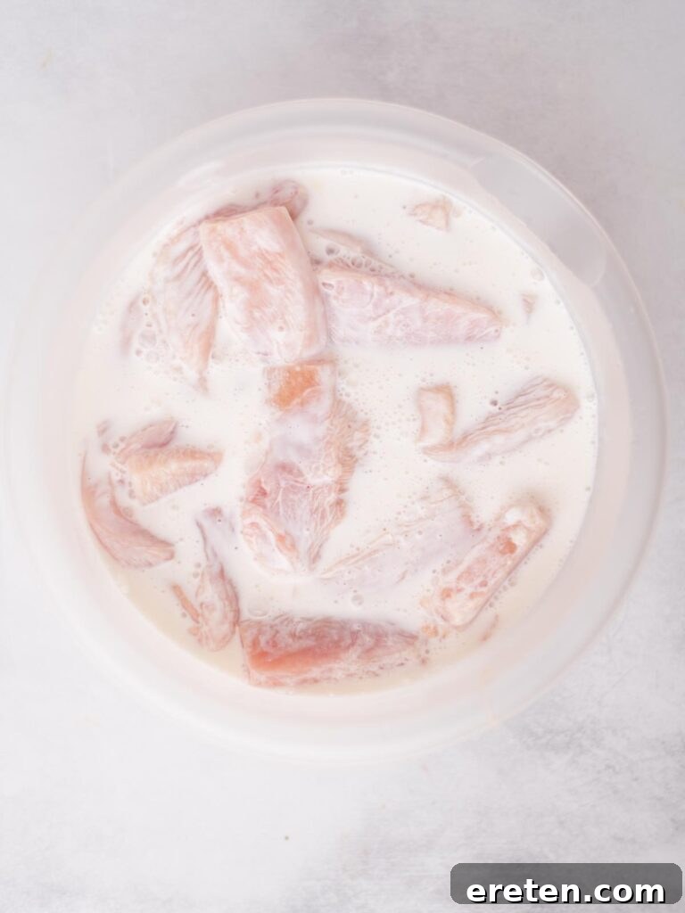 Raw chicken pieces marinating in buttermilk within a mixing bowl, ready for flavor infusion.