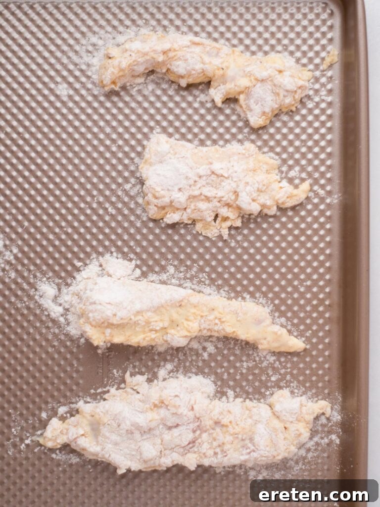 Chicken pieces, thoroughly coated in seasoned flour, neatly arranged on a baking sheet, ready for chilling.