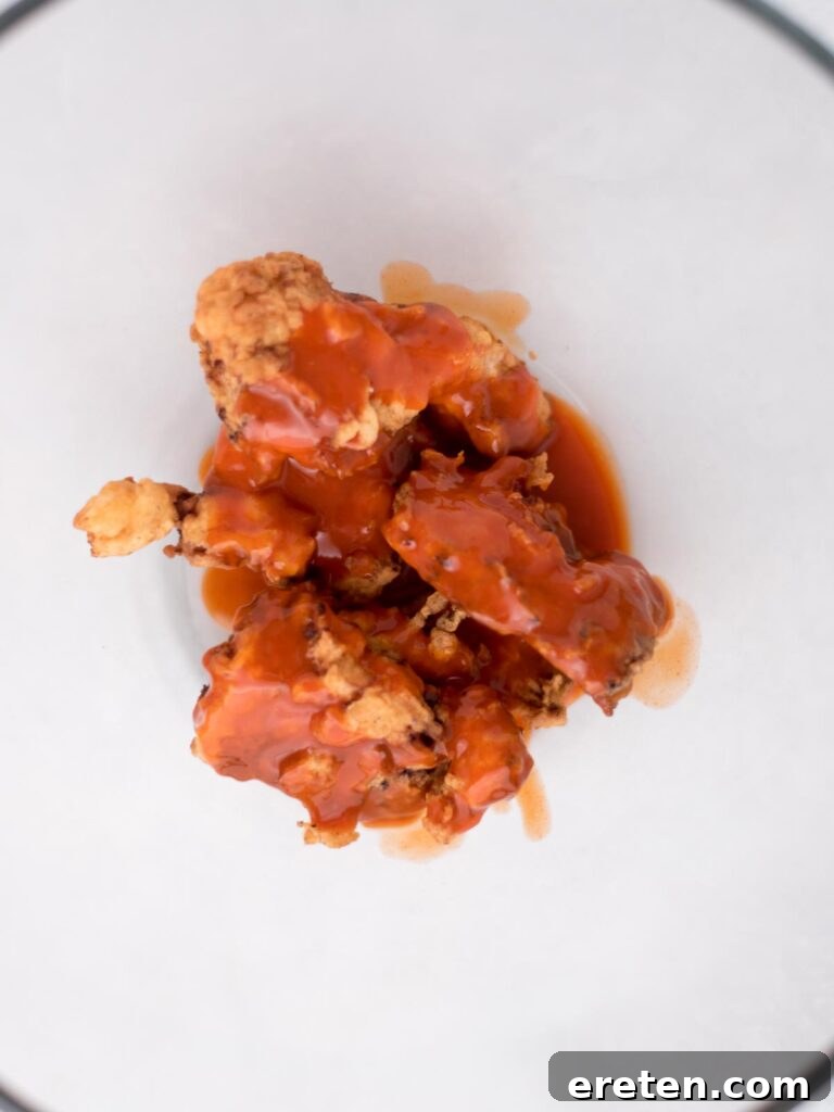 Golden-fried boneless wings being tossed in a mixing bowl with buffalo sauce, ensuring every piece is evenly coated.