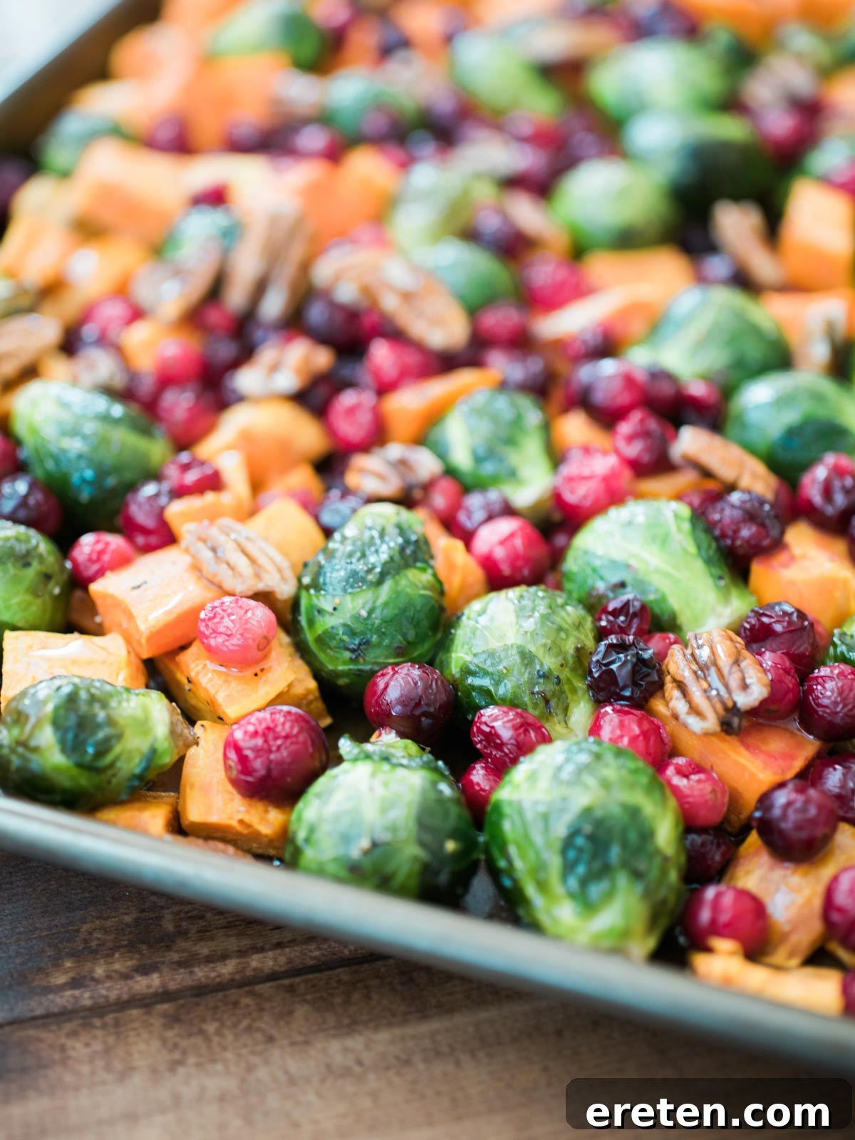 Assorted honey-roasted vegetables, including Brussels sprouts, butternut squash, cranberries, and pecans, spread on a baking sheet, glistening with honey and ready to serve.