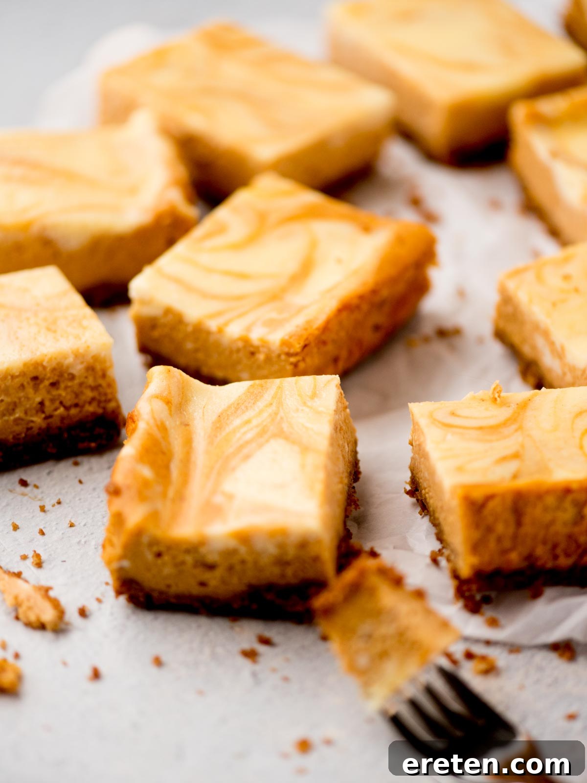 Delicious pumpkin cheesecake bars arranged on parchment paper, with one bar showing a bite taken from a fork, highlighting its creamy texture.