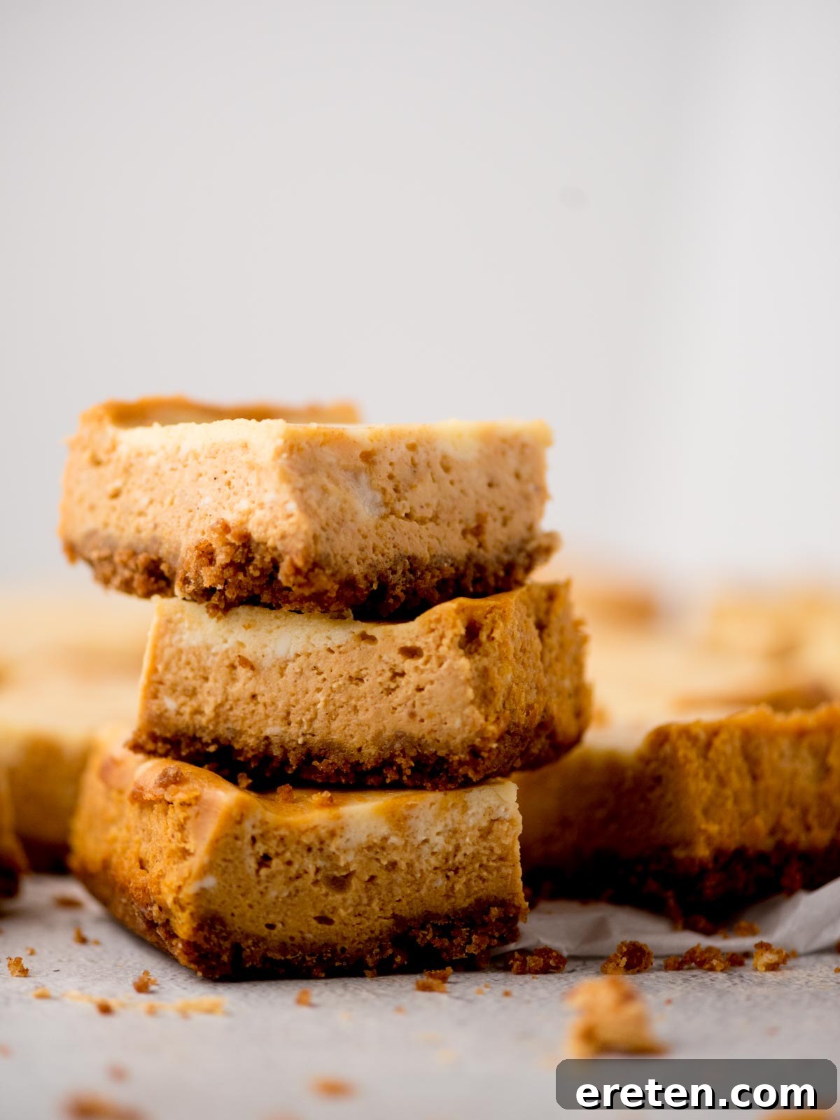 Three perfectly baked pumpkin cheesecake bars, stacked on top of each other, showcasing their layers and creamy texture.