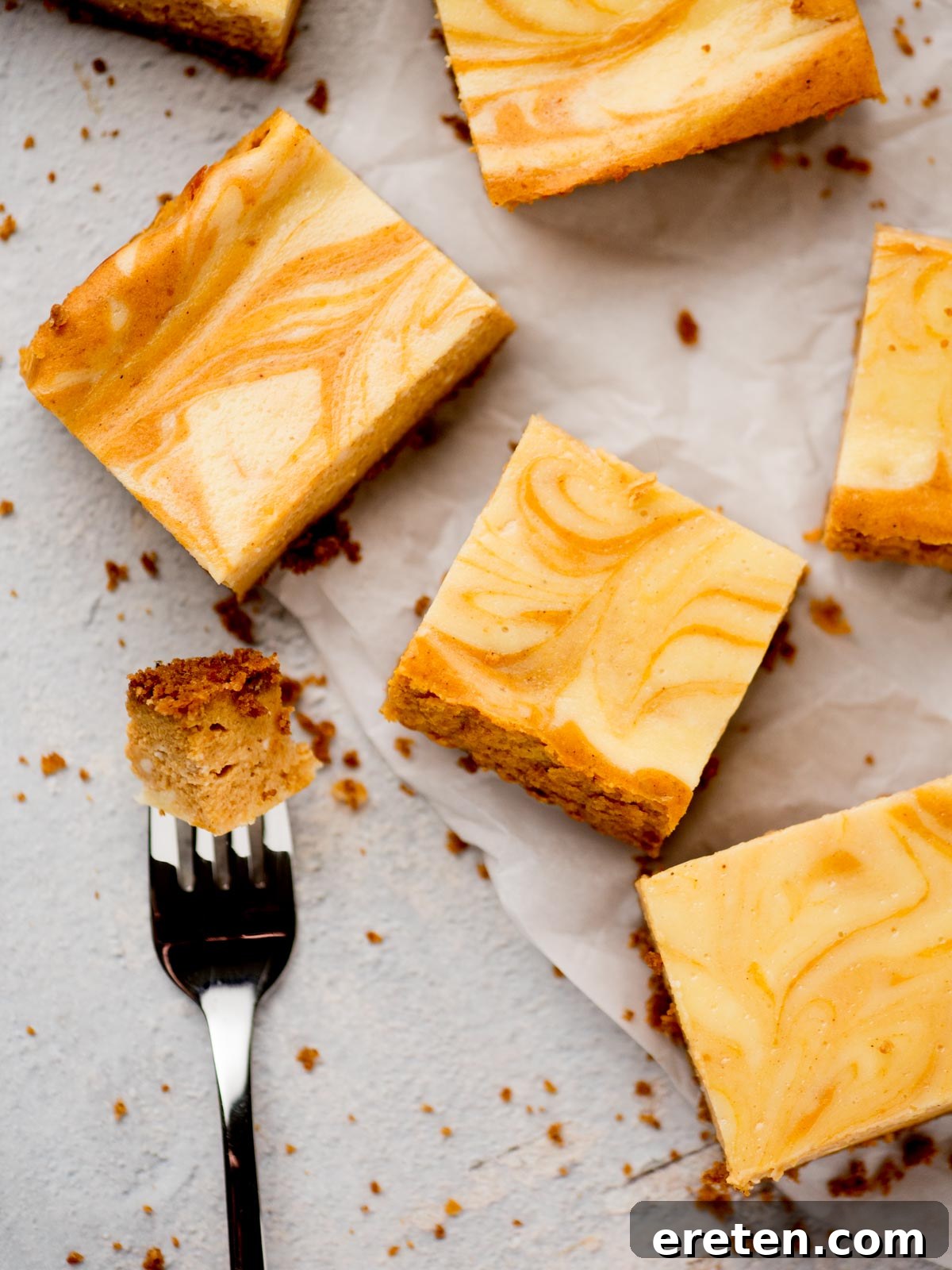 Close-up of a pumpkin cheesecake bar on parchment paper, showing the beautiful swirl and a bite on a fork, emphasizing its creamy texture.