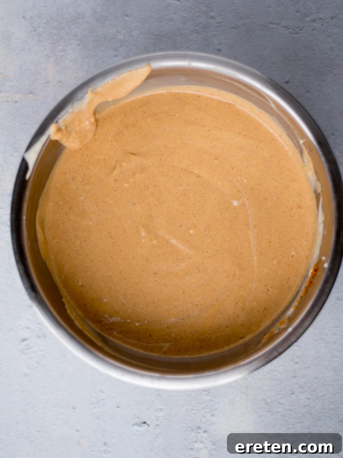 Pumpkin cheesecake filling, mixed with spices, in a bowl, showing its warm orange hue.