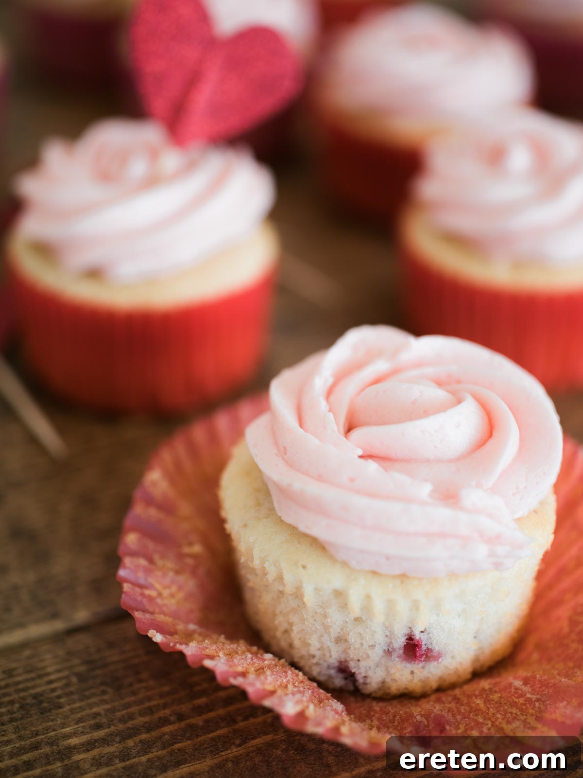 A single strawberry vanilla cupcake, with its liner partially peeled, showcasing the tender cake and luscious strawberry buttercream.