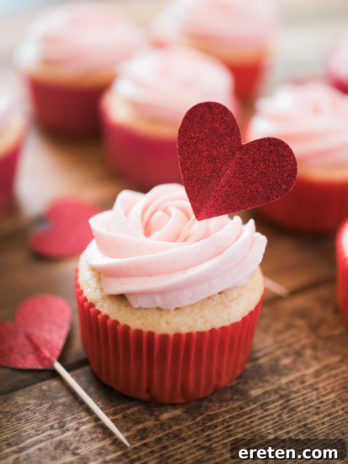 A beautifully decorated strawberry vanilla cupcake topped with a charming heart decoration, ready to be enjoyed.