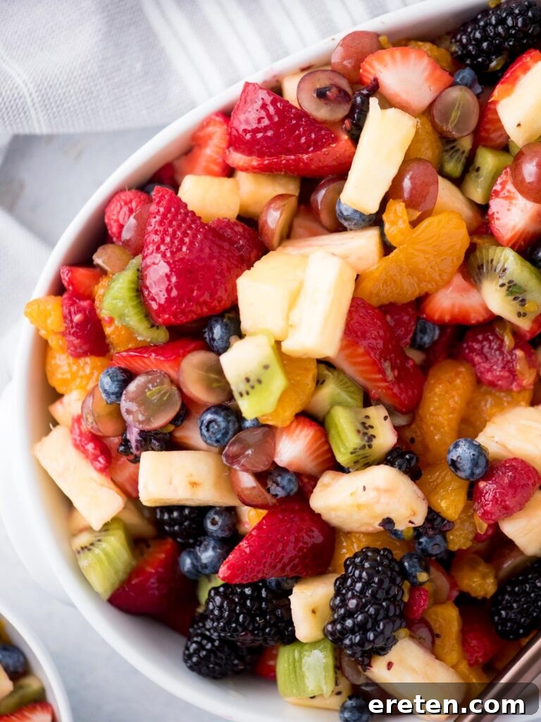 A beautifully arranged fruit salad in a pristine white bowl, accompanied by a graceful serving utensil, showcasing an array of colorful and juicy fresh fruits.