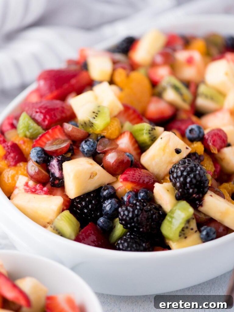 A vibrant and generously portioned fruit salad, glistening with its sweet citrus dressing, presented beautifully in a white bowl with a serving utensil, promising a refreshing culinary delight.
