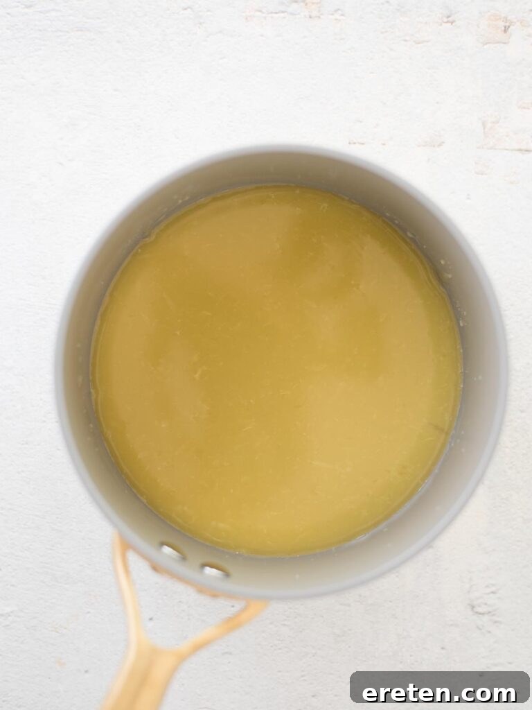 A sweet citrus dressing gently simmering and cooling in a saucepan, ready to be poured over a medley of fresh fruits.