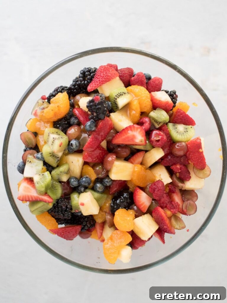 A generous amount of sweet citrus dressing cascading over a colorful assortment of mixed fresh fruits in a large, inviting mixing bowl, ready to be gently tossed.