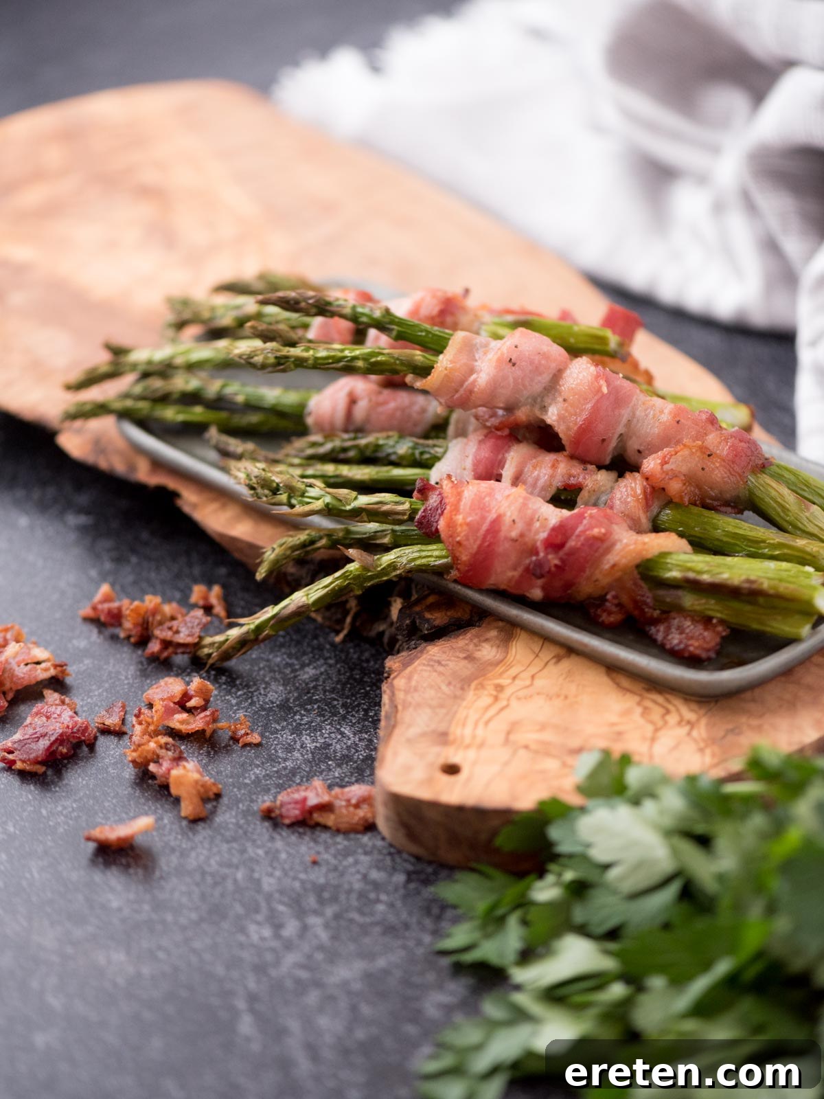 Crispy Air Fryer Bacon Asparagus Bundles 2 Platter of bacon wrapped asapargus with crispy bacon pieces around the edge.
