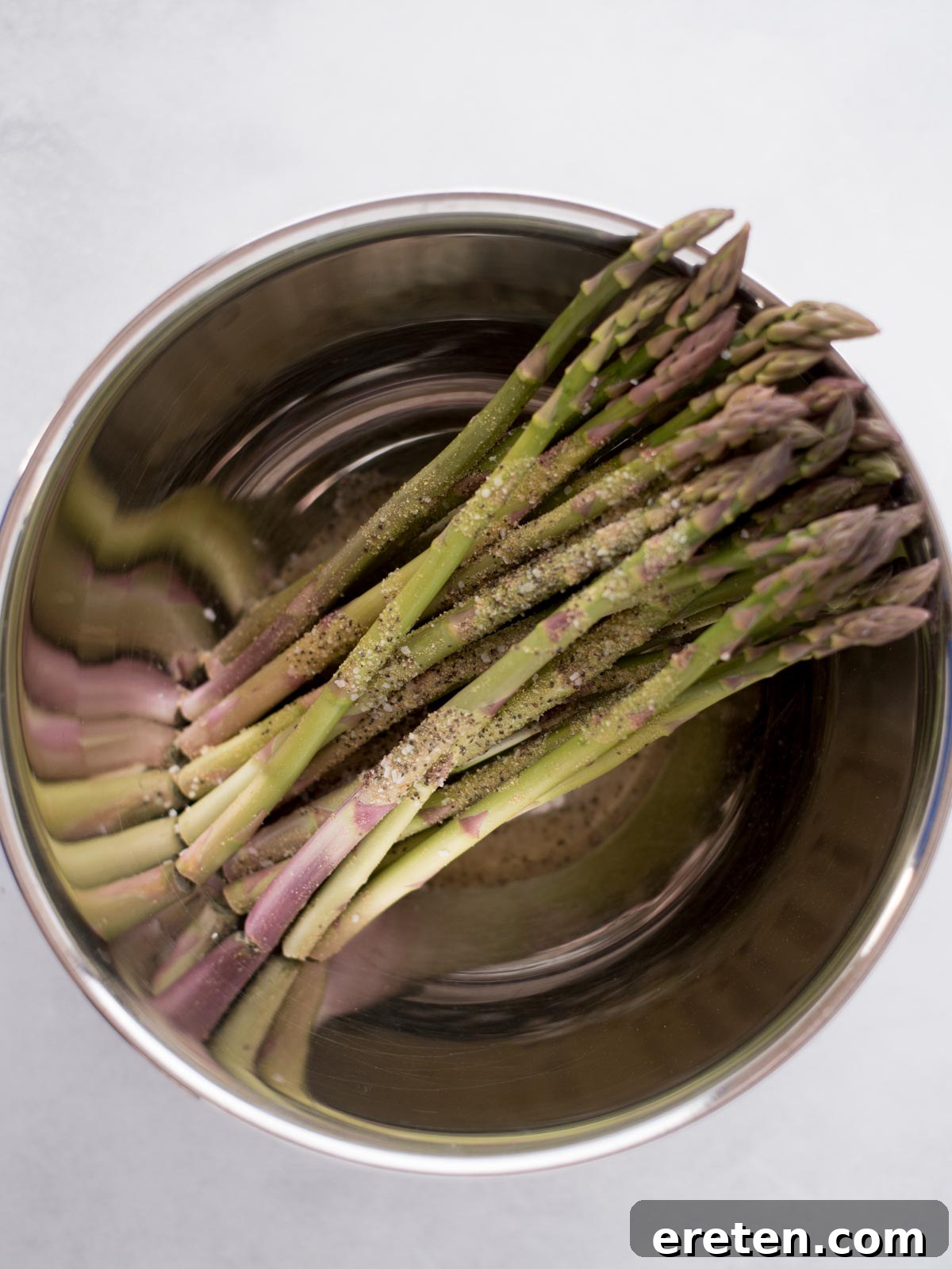 Crispy Air Fryer Bacon Asparagus Bundles 3 Seasoned asparagus in a mixing bowl.