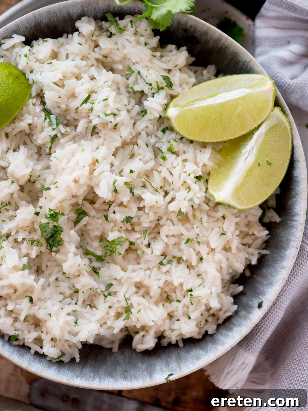 A beautifully presented bowl of cilantro lime rice, garnished generously with fresh cilantro leaves and bright green lime wedges.