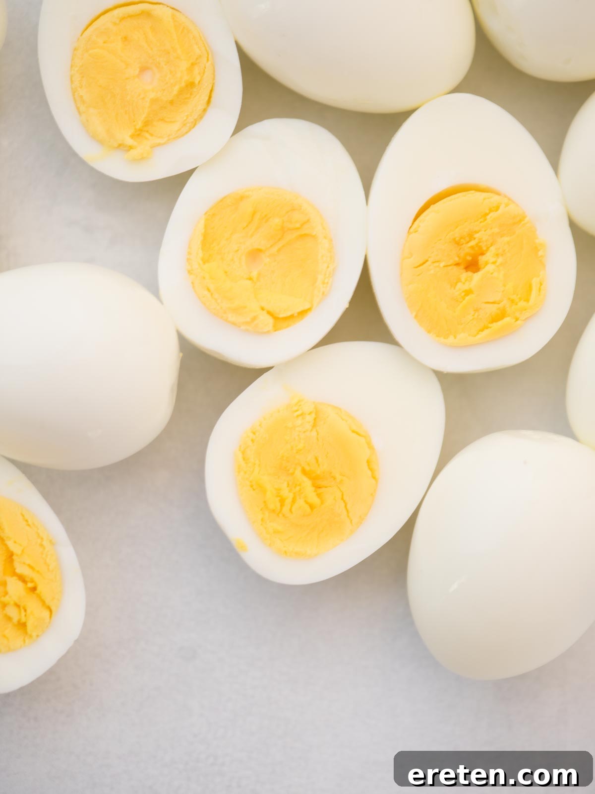 A selection of whole and perfectly hard-boiled eggs, some halved to reveal creamy, vibrant yellow yolks.