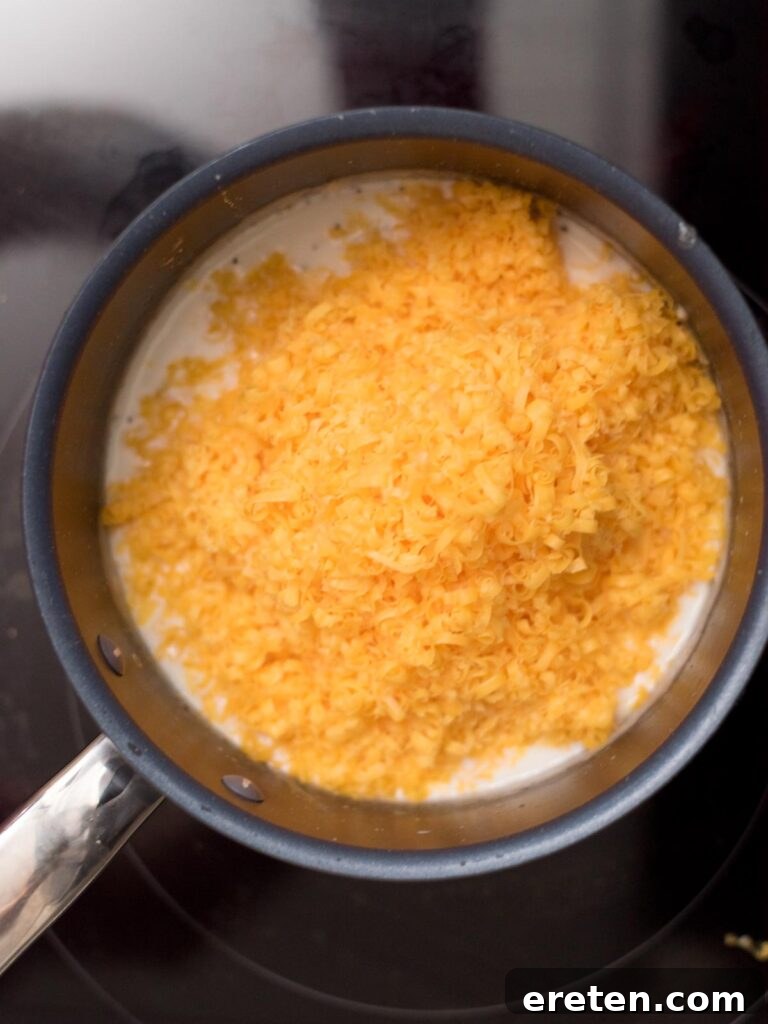 Hand shredded cheese added to a saucepan.
