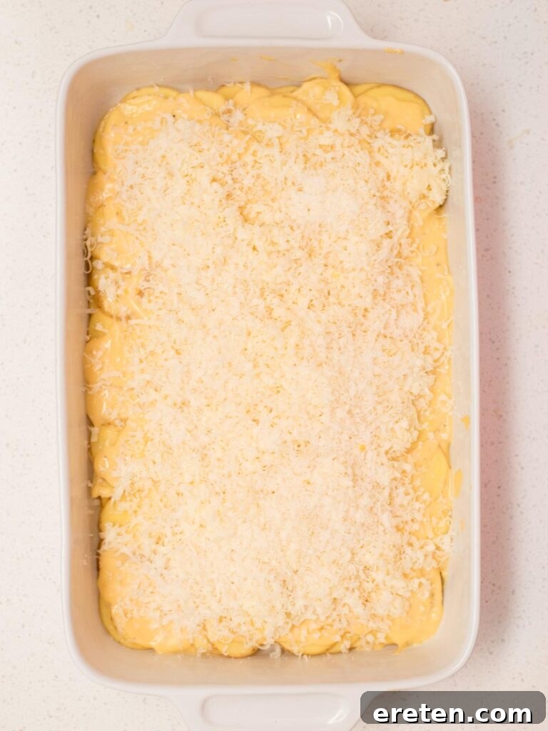 Potatoes layered in a casserole dish and topped with grated cheese.