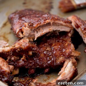 Close up of ribs on a baking sheet with sauce coating them and a few pieces of lean meat pulled away.