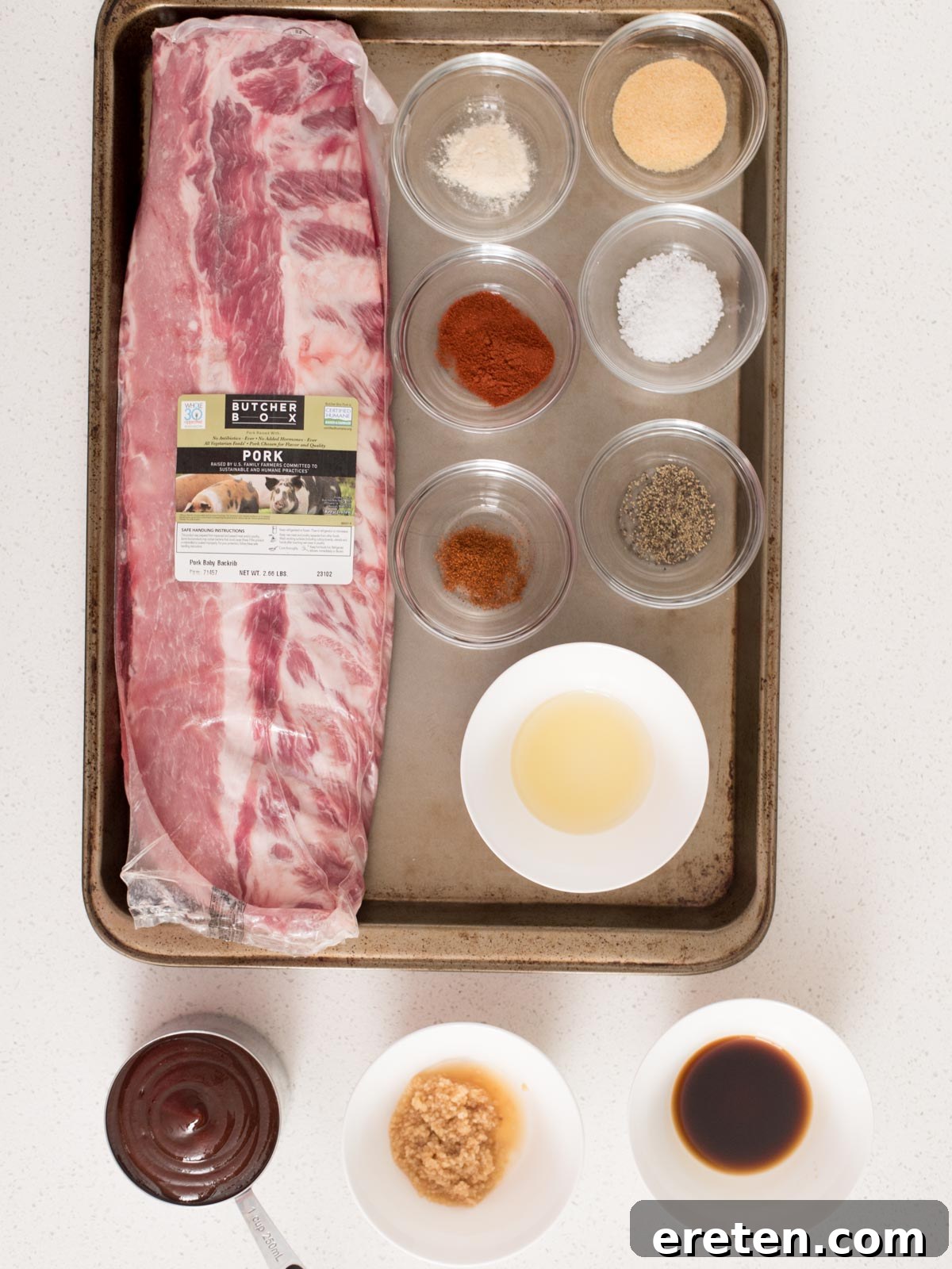 A selection of ingredients for oven-baked ribs, including spices, a rack of ribs, and barbecue sauce.
