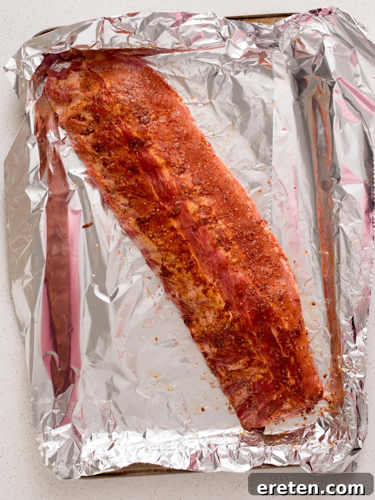 Raw pork ribs coated in a rich dry rub seasoning, ready for baking.