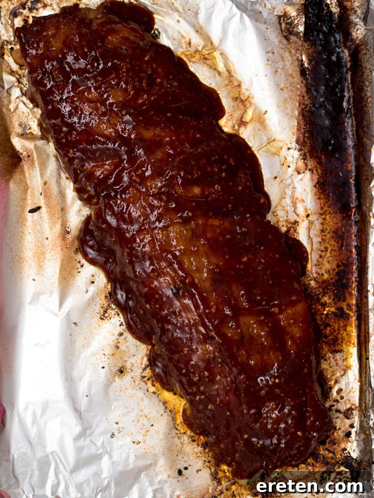 Barbecue sauce being brushed onto cooked pork ribs.