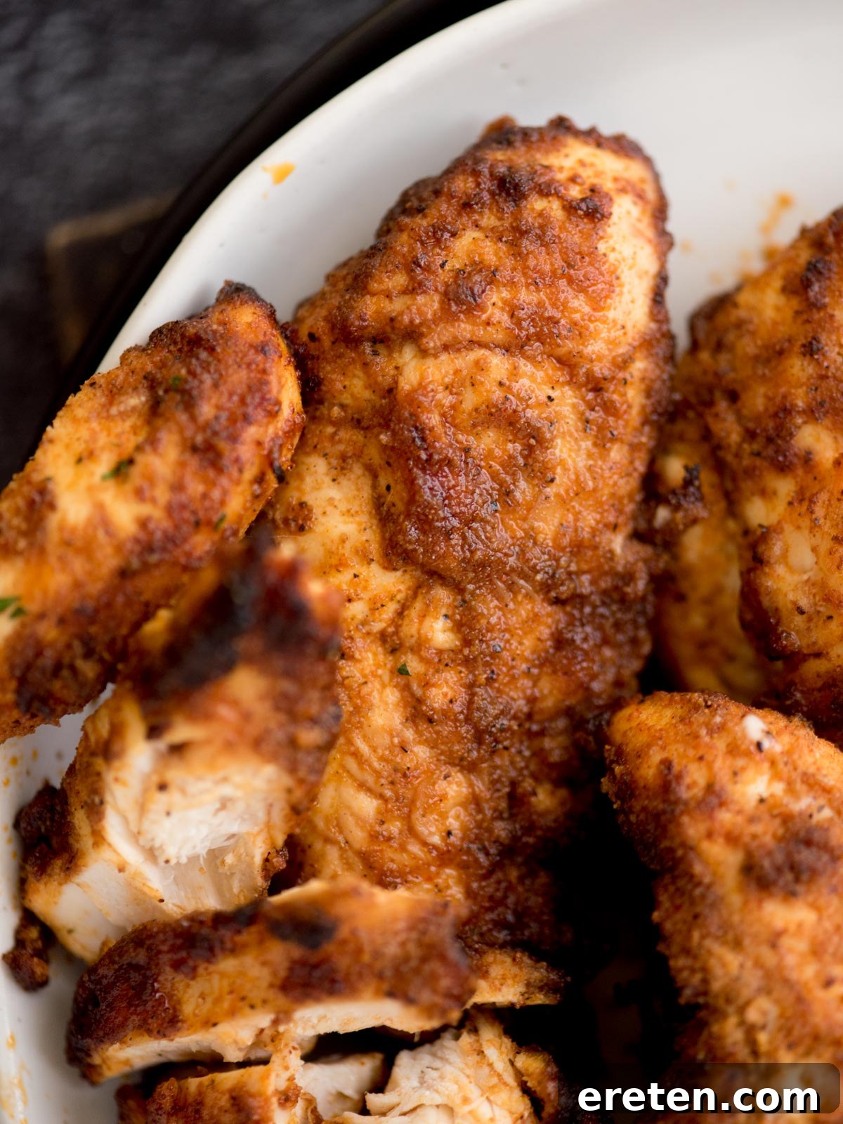 Close-up view of perfectly golden-brown and crispy air fryer chicken tenders on a plate, showcasing their inviting texture and rich seasoning against a soft, blurred background, highlighting their appetizing appearance.