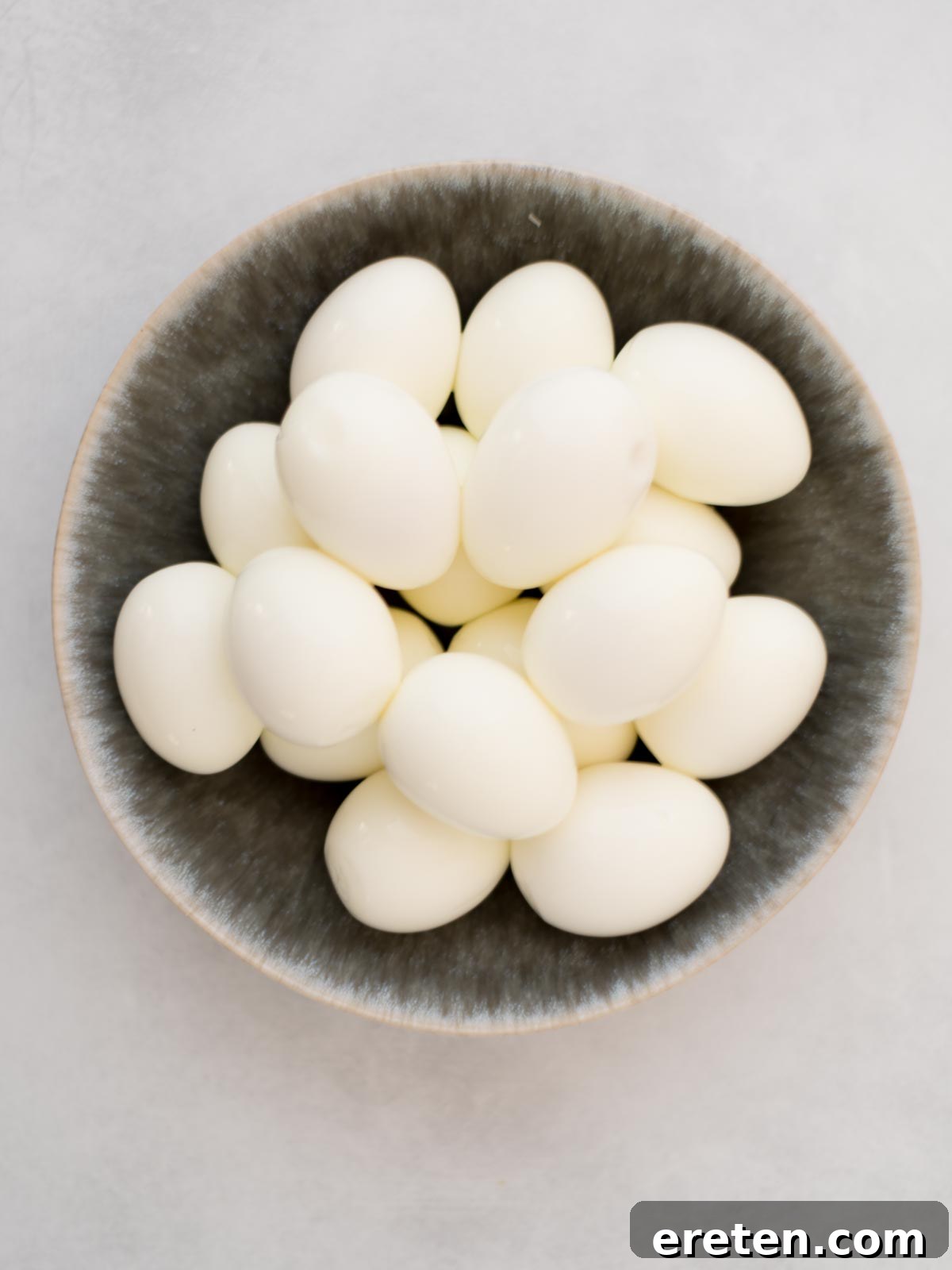 A hard-boiled egg being cut in half lengthwise with a knife.