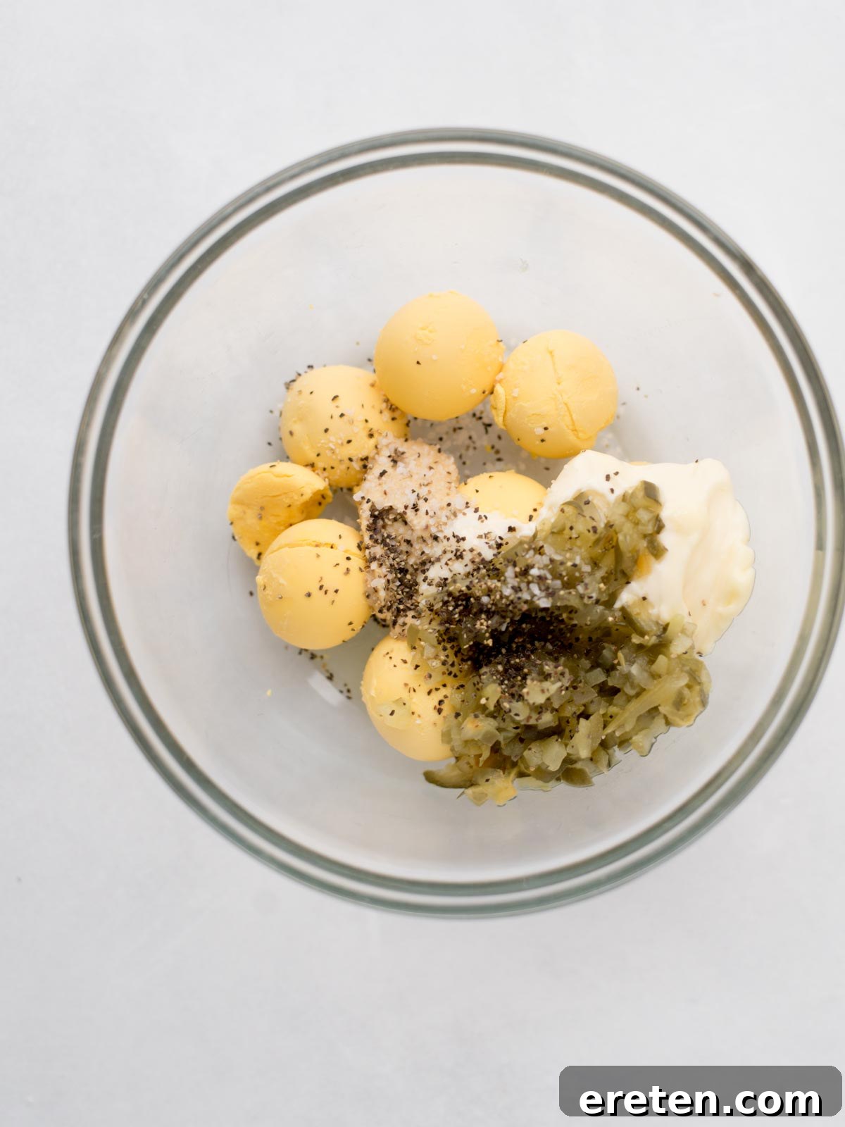 Mashing egg yolks and other ingredients together in a mixing bowl.