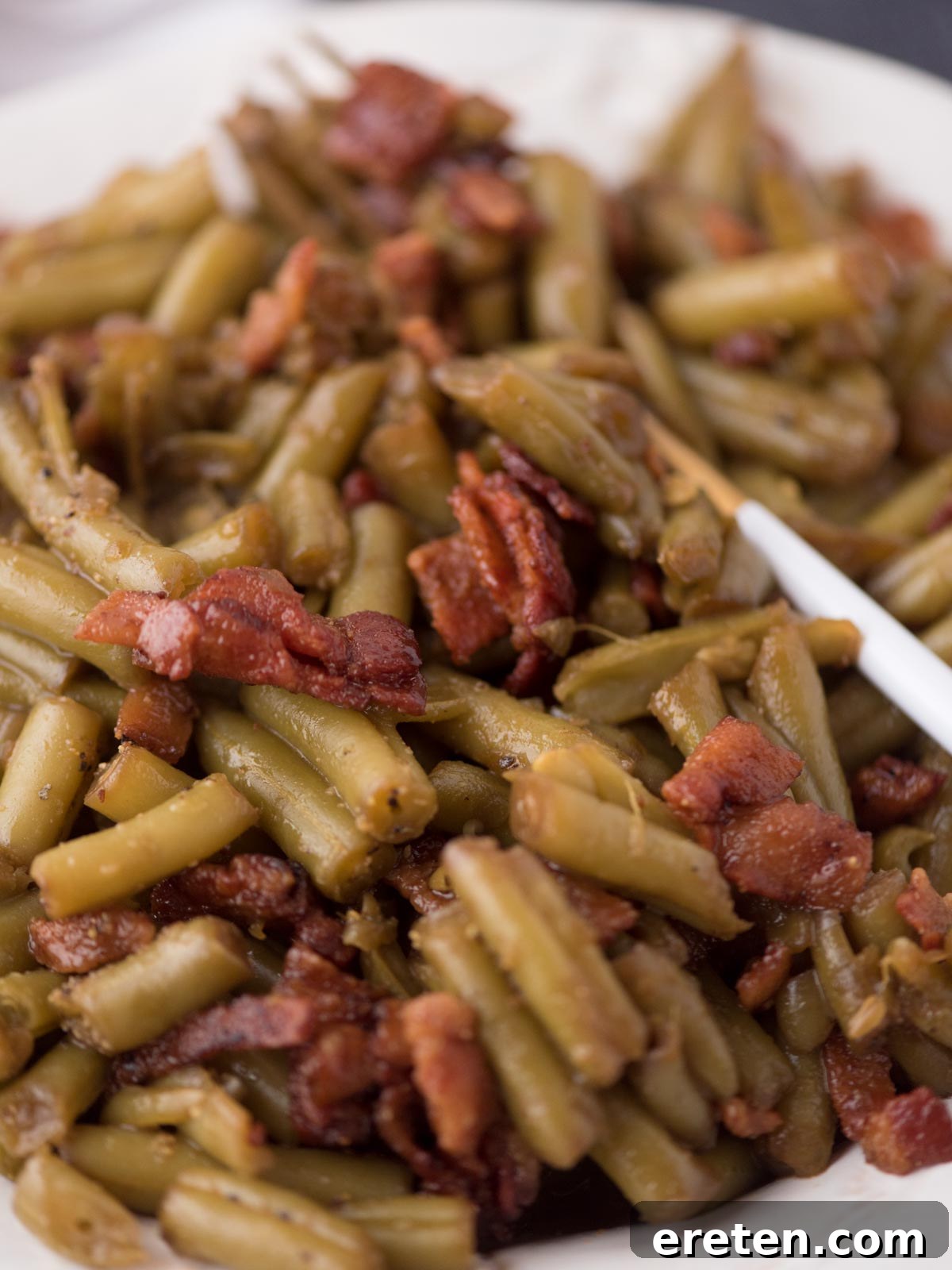 A close-up of a serving of crack green beans with bacon on a plate, ready to be eaten.