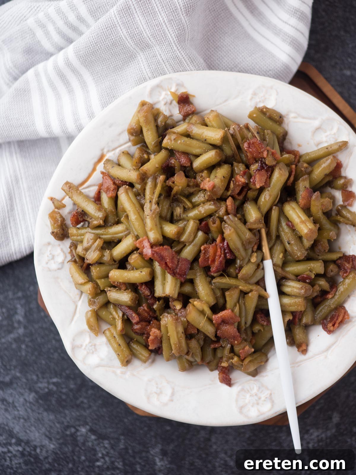A top-down shot of the finished crack green beans with bacon, garnished and ready to serve in a skillet.