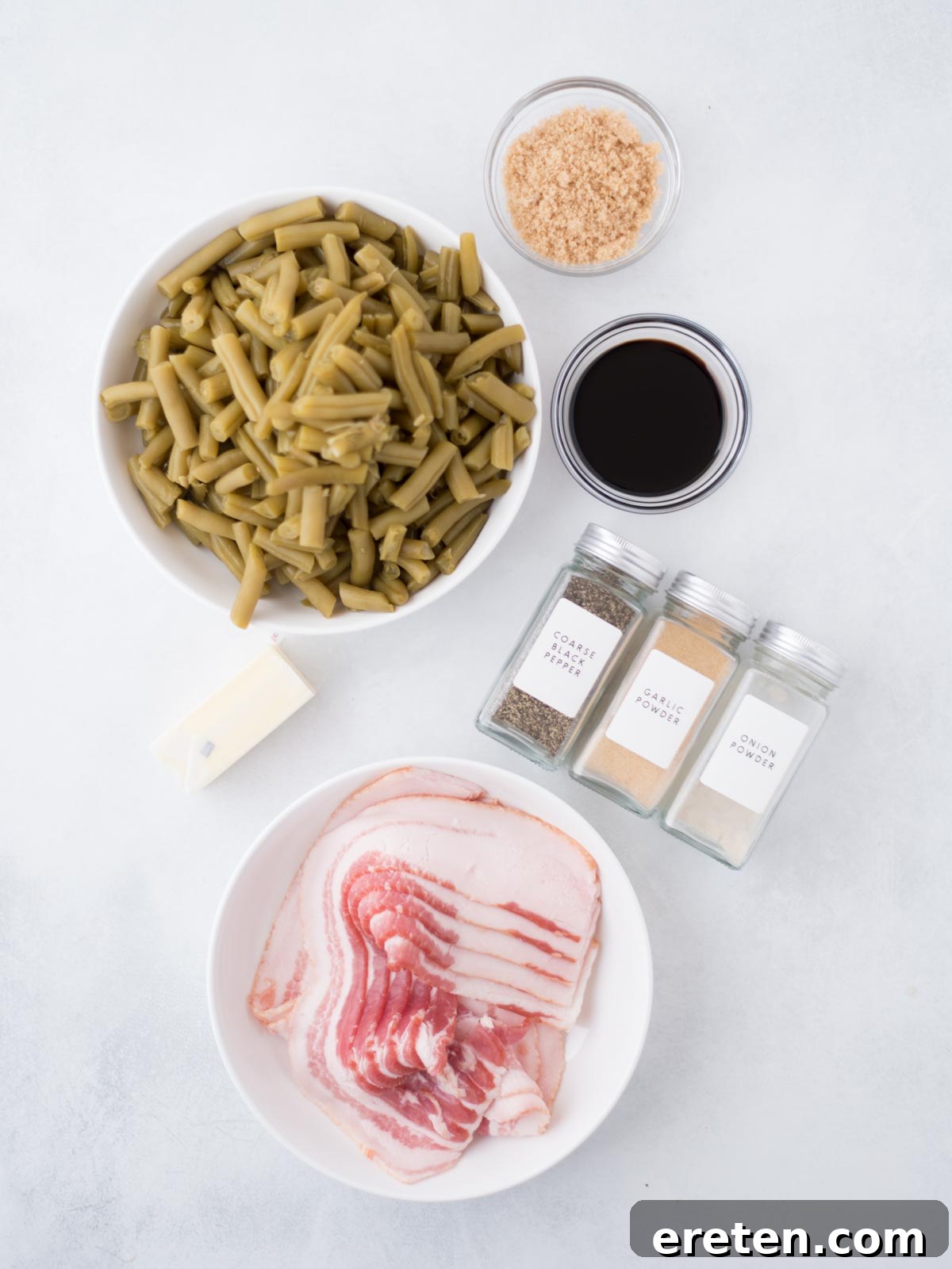 A close-up of the fresh ingredients laid out on a wooden board, including canned green beans, thick-cut bacon, butter, brown sugar, soy sauce, garlic powder, onion powder, and black pepper.