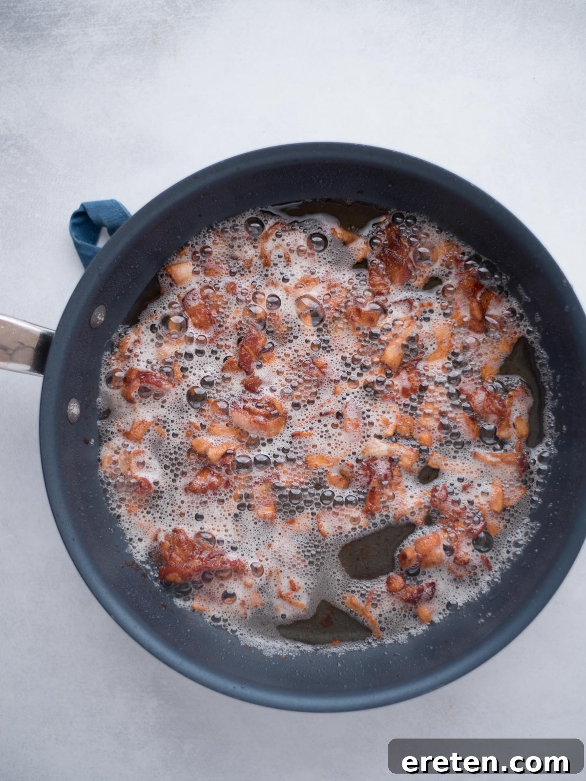 Chopped thick-cut bacon sizzling in a large cast iron skillet, cooking until crispy.