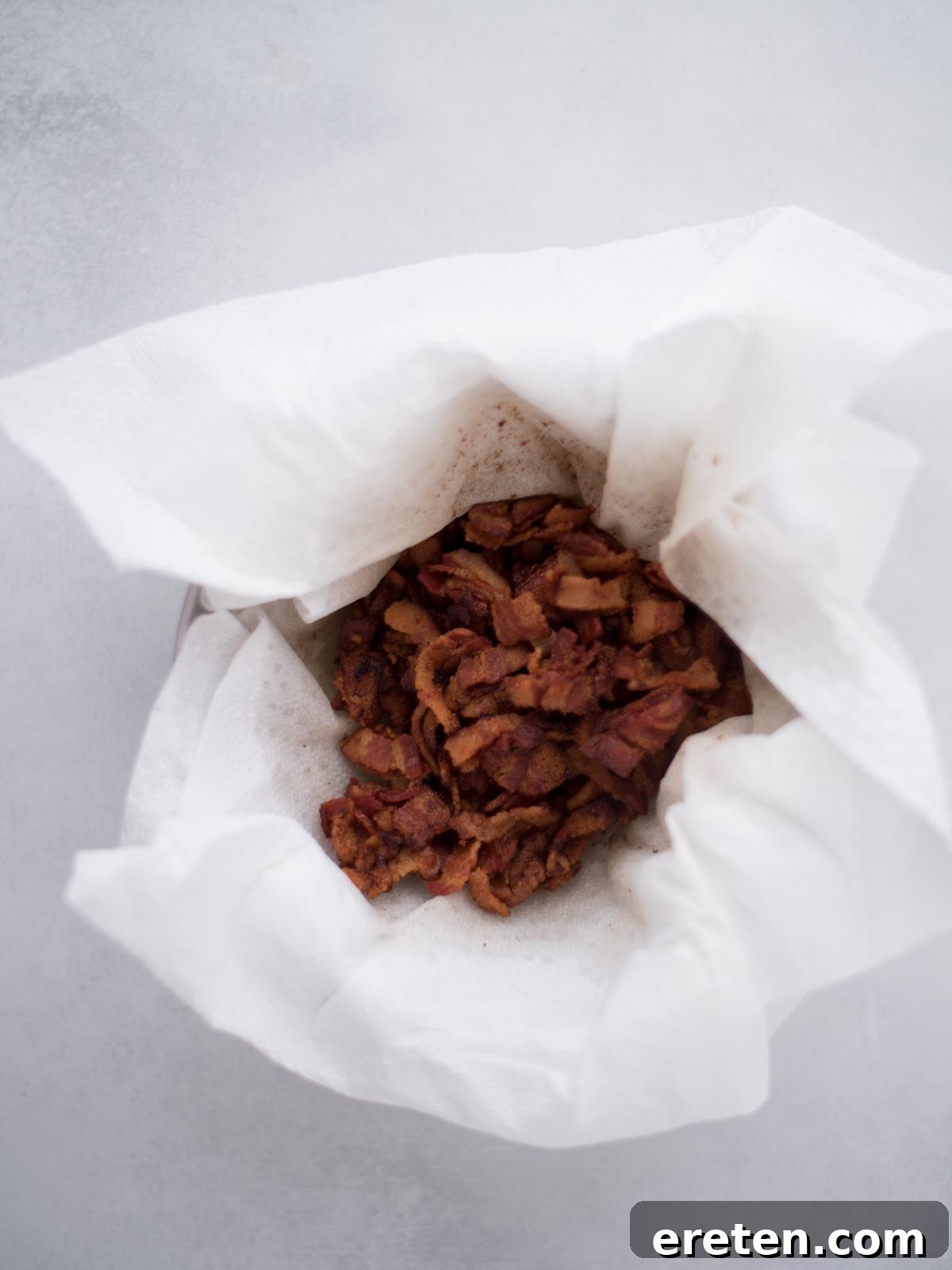Crispy cooked bacon pieces draining on a paper towel-lined plate.