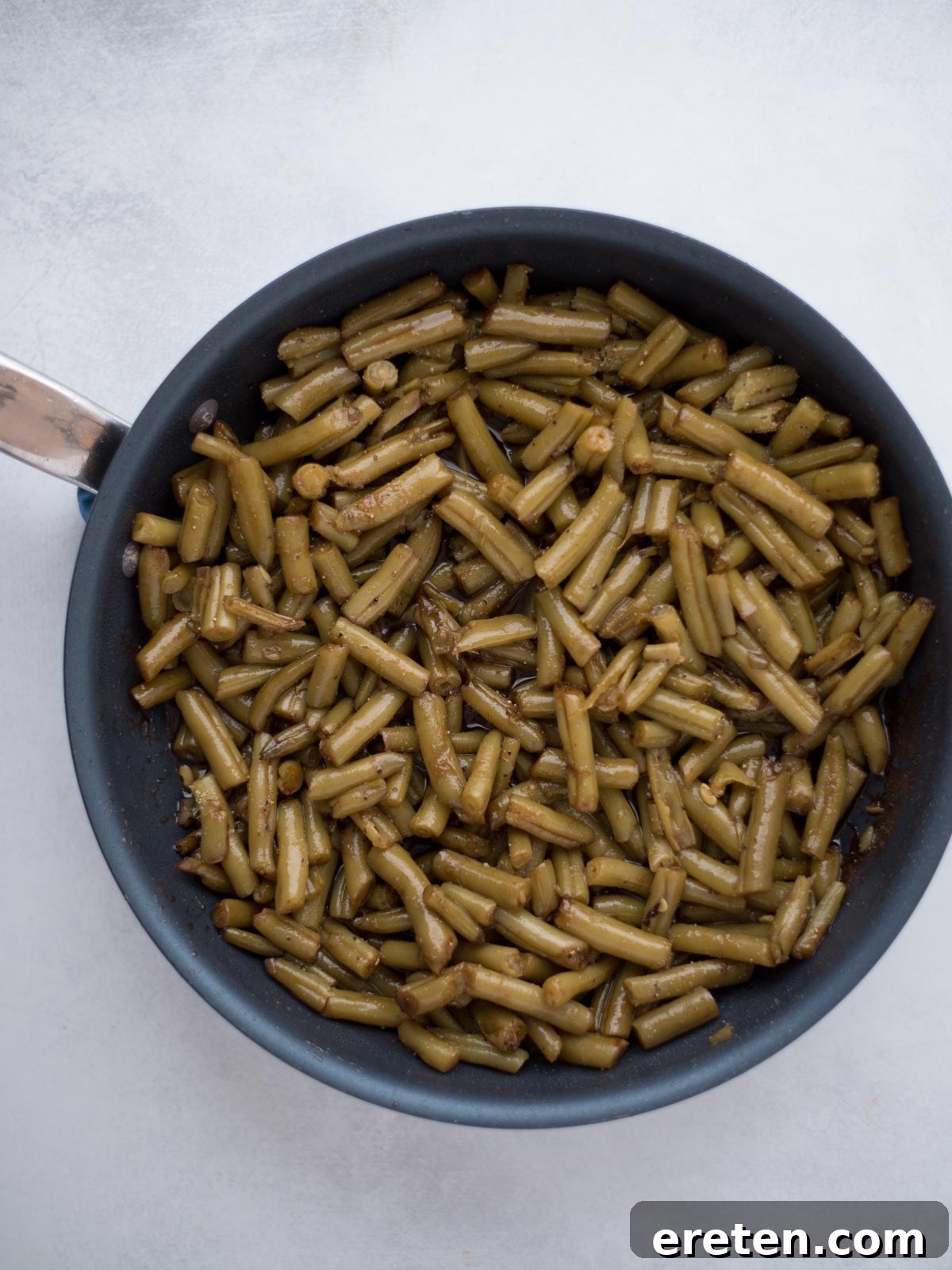 Drained green beans added to the simmering glaze in the skillet, ready to be seasoned.