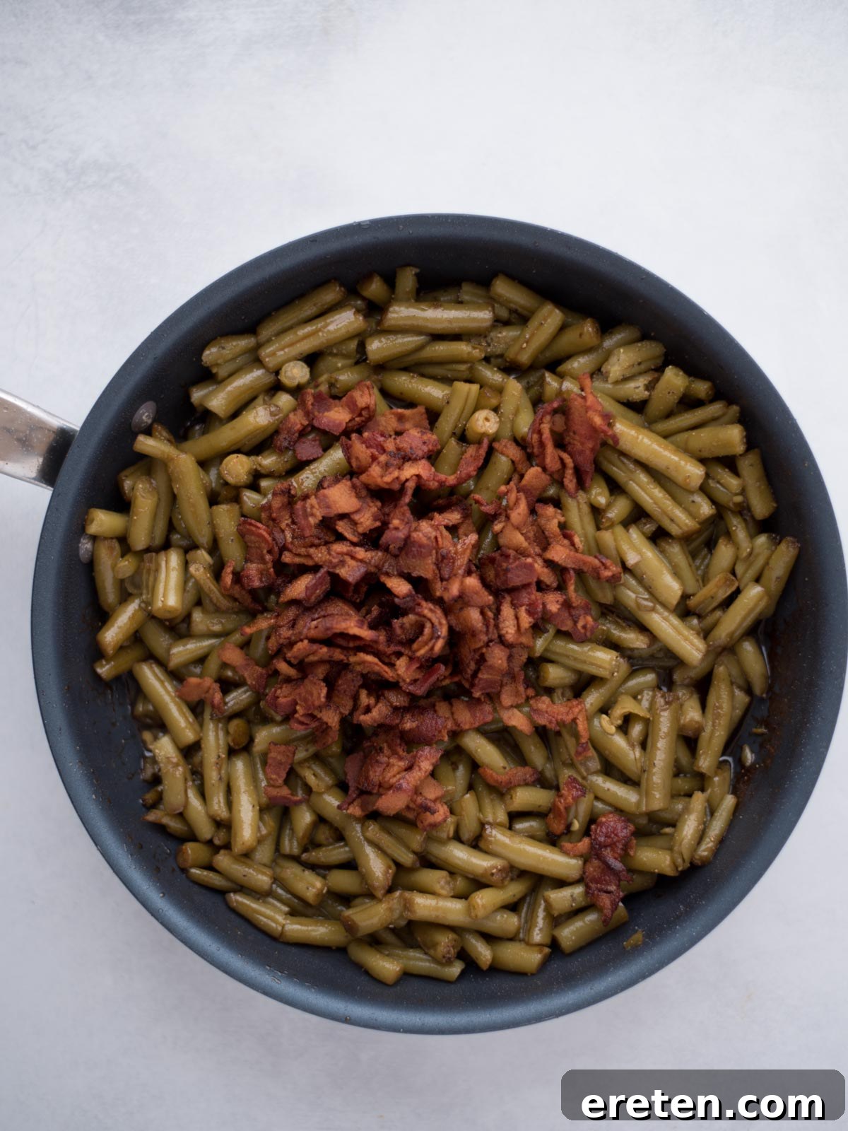 Crispy bacon bits mixed into the glazed green beans in the skillet, ready to serve.