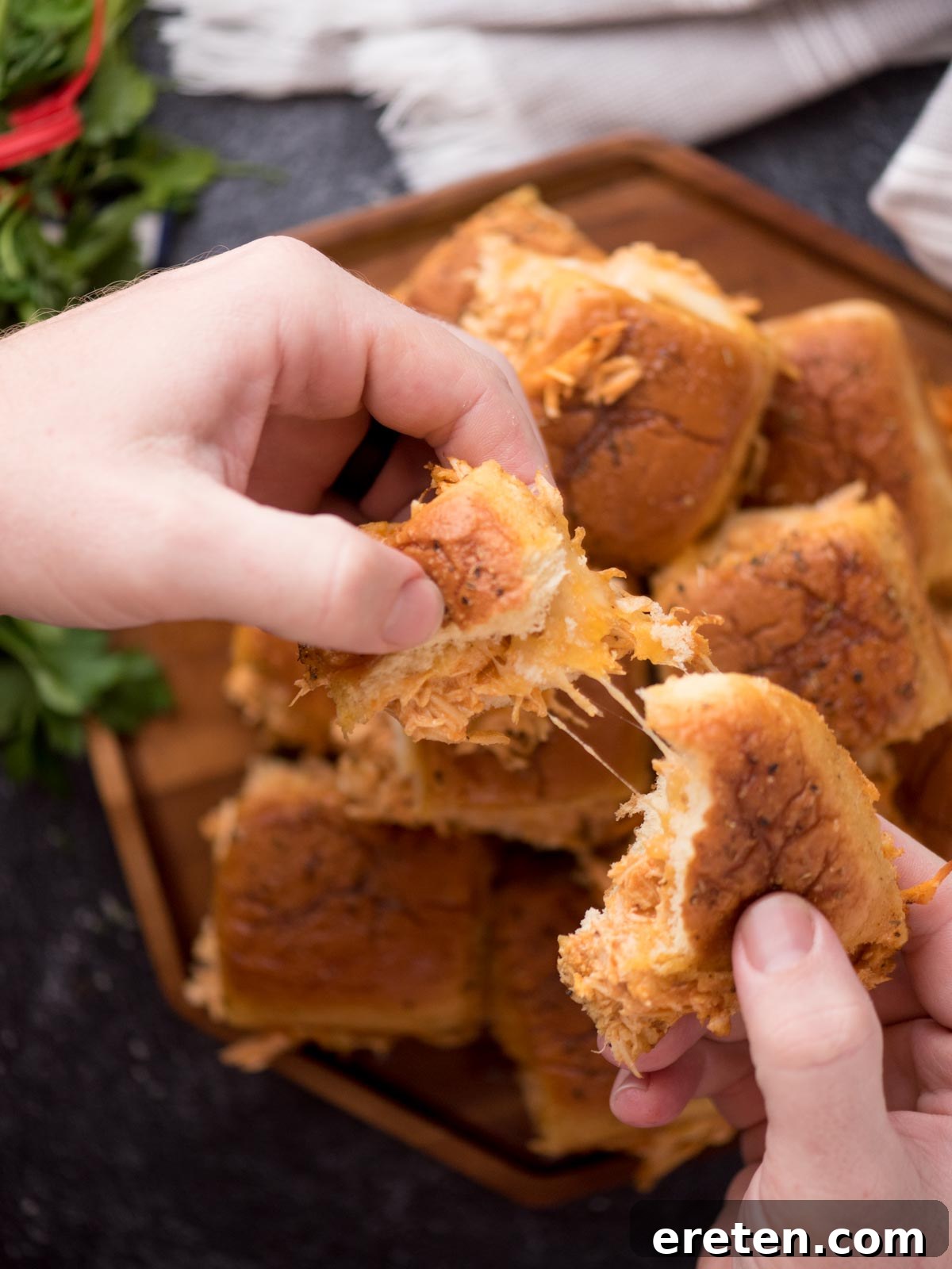 Hand pulling apart a cheesy buffalo chicken slider.