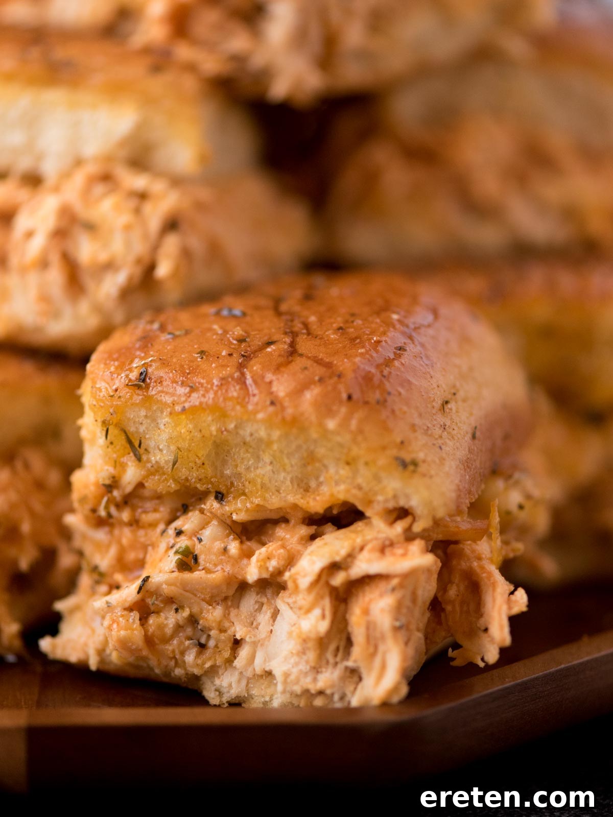 A single buffalo chicken slider with seasoned chicken spilling out sitting on a platter of sliders.