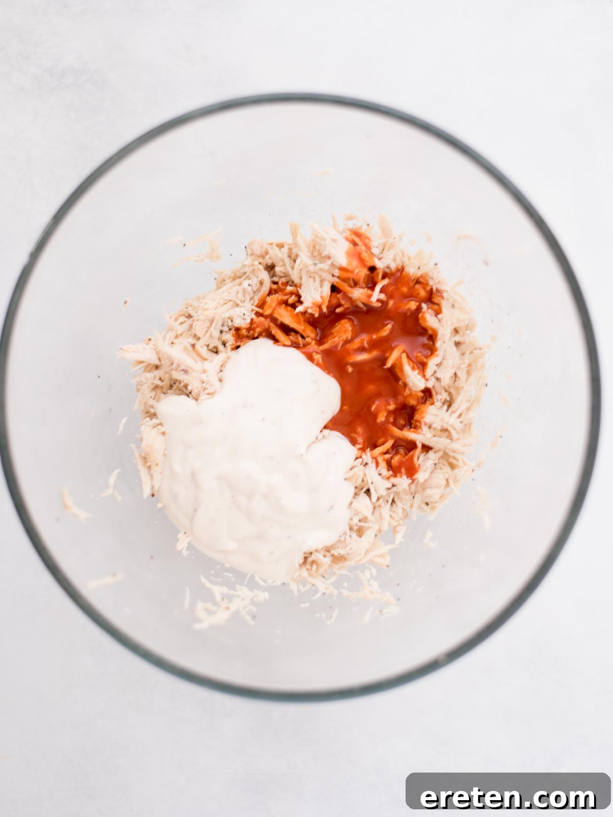 Shredded chicken in a bowl with seasonings measured out over top of it.