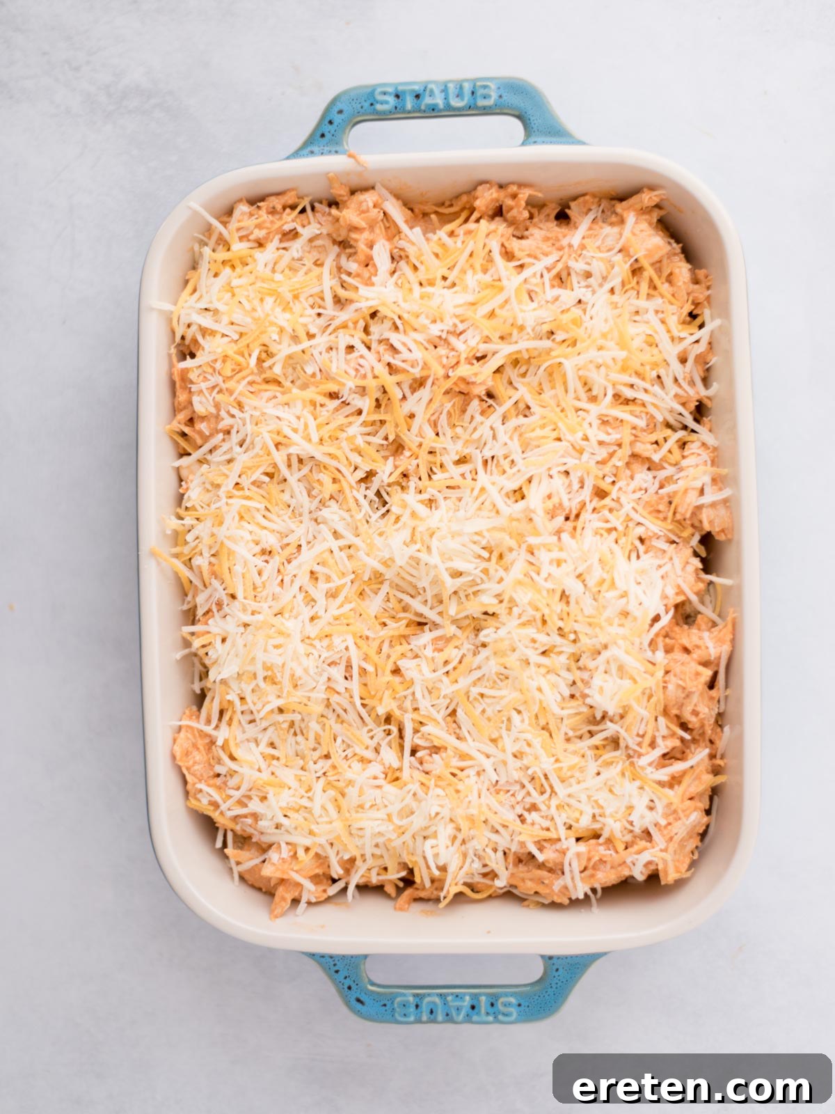 Shredded cheese topping the buffalo chicken sliders in a baking dish.