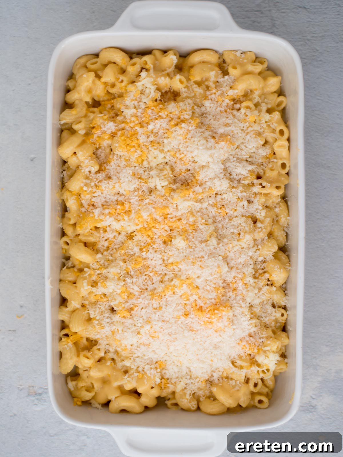 Mac and cheese in a baking dish with a generous, golden sprinkle of shredded Gruyere and Parmesan cheese on top, anticipating its bake.