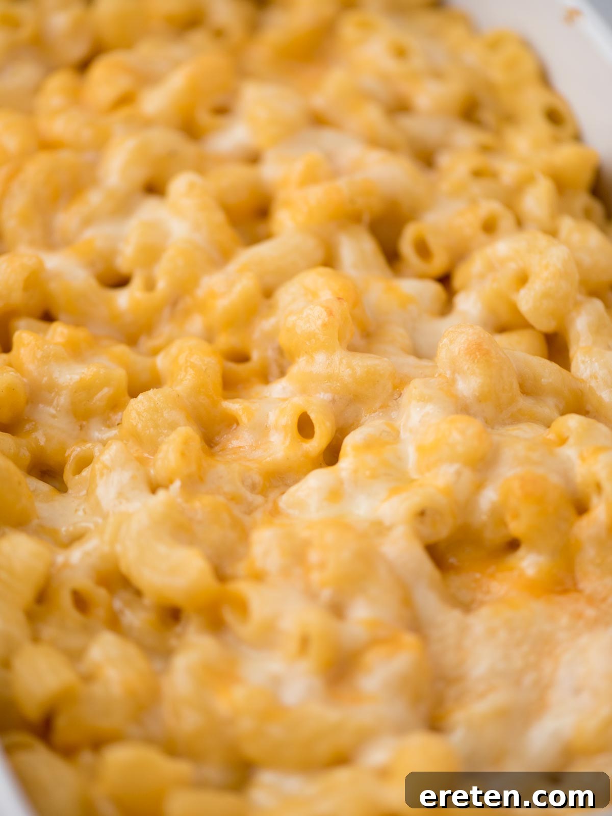 A close-up shot of a serving of baked mac and cheese, showcasing its creamy texture, visible melted cheese, and a hint of golden crust. The focus is on the rich, indulgent nature of the dish.