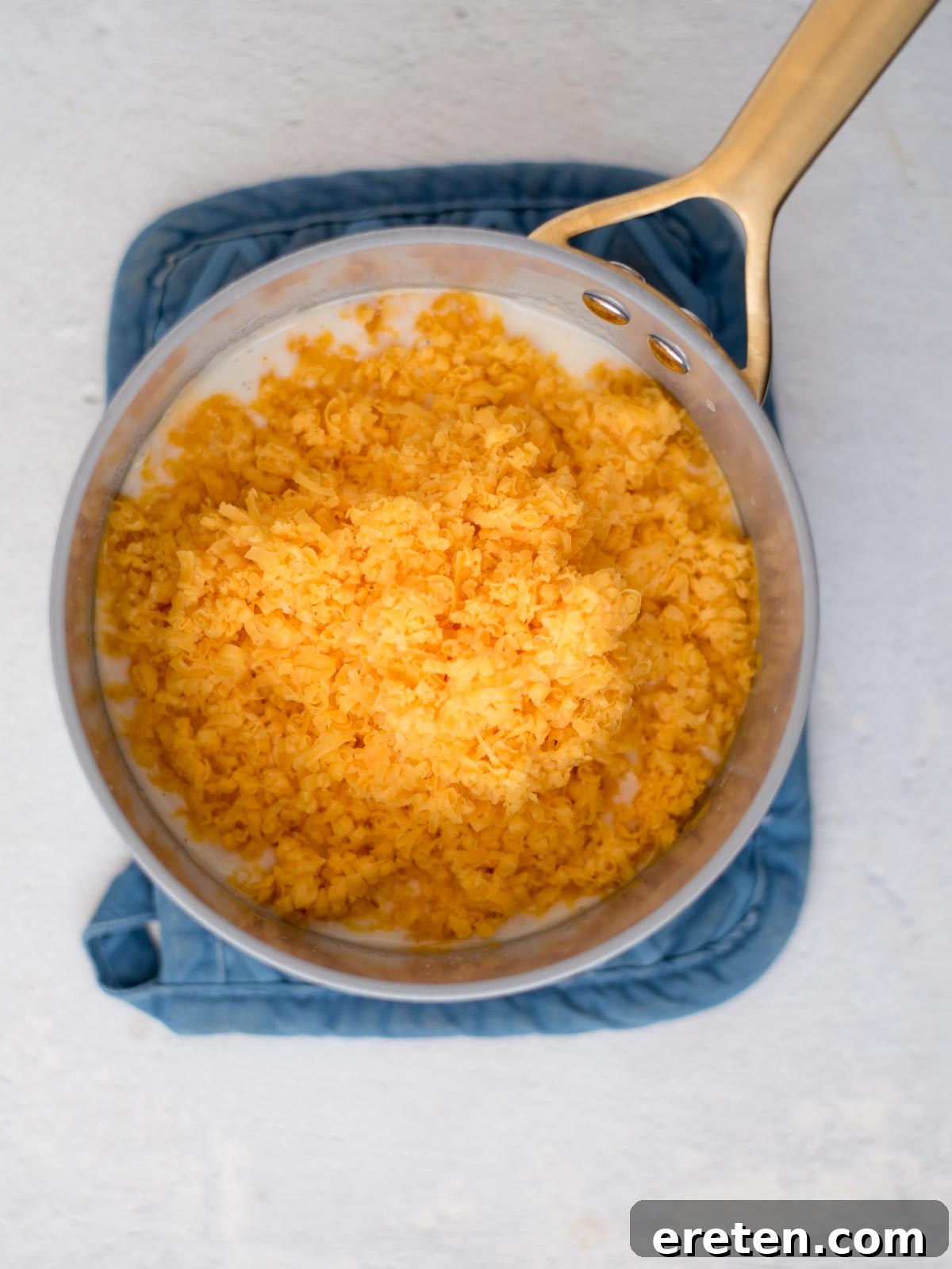 A generous handful of freshly shredded cheese being carefully added to a simmering white sauce in a saucepan, ready to melt into creamy perfection.