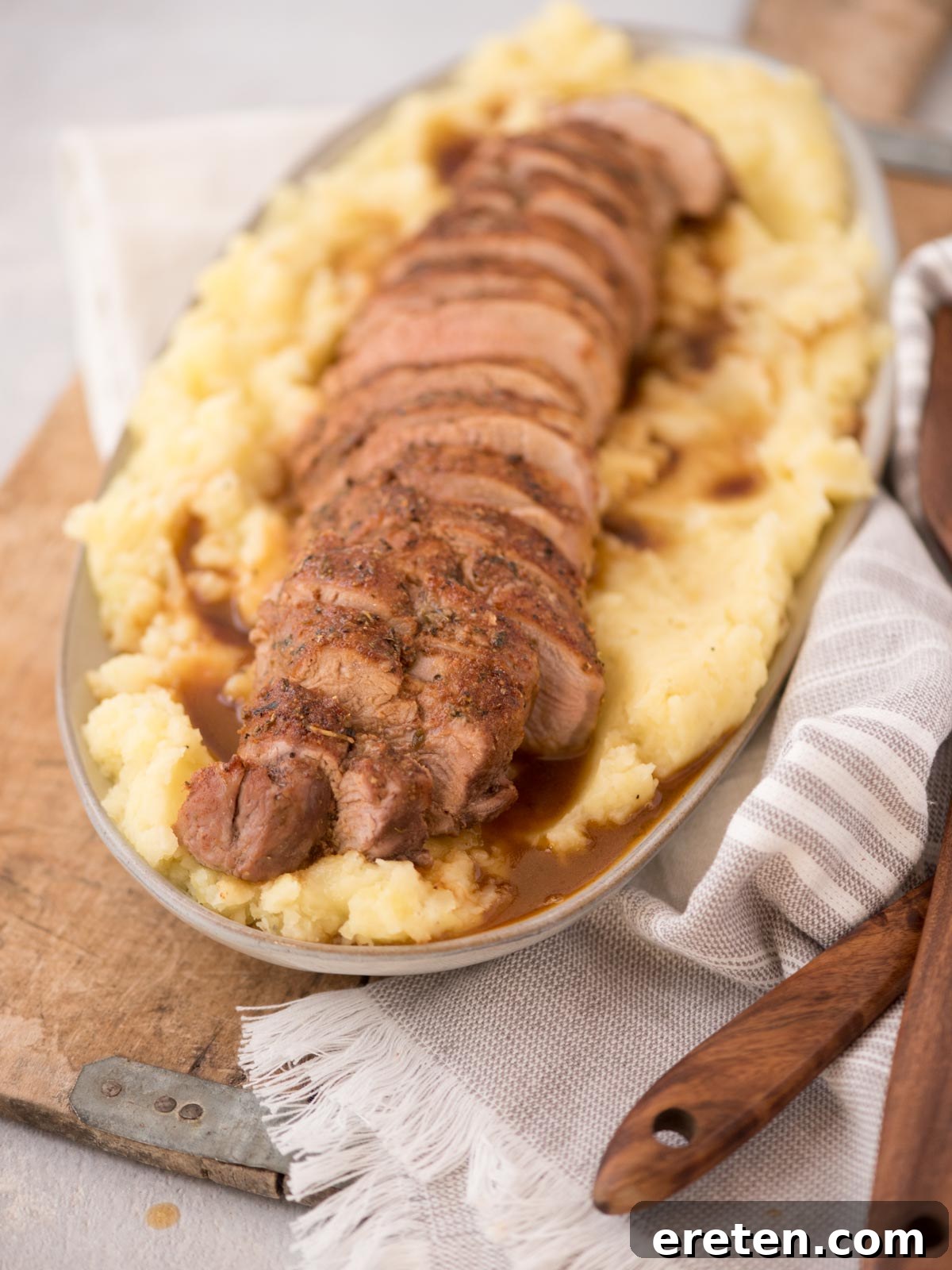 Sliced, golden-brown pork tenderloin resting atop a bed of creamy mashed potatoes, ready for serving on an elegant platter.