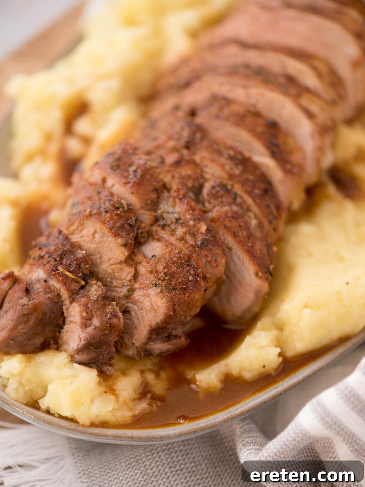 Generously sliced roast pork tenderloin artfully arranged over a bed of creamy mashed potatoes on a sophisticated serving platter.