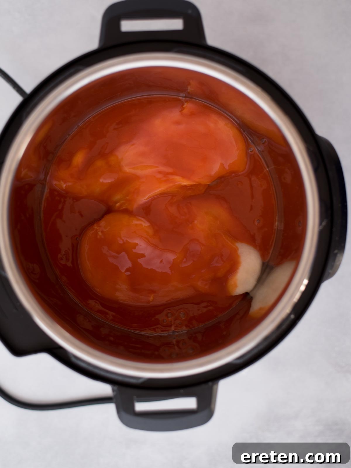 Buffalo sauce and raw chicken breasts inside the instant pot ready to cook.