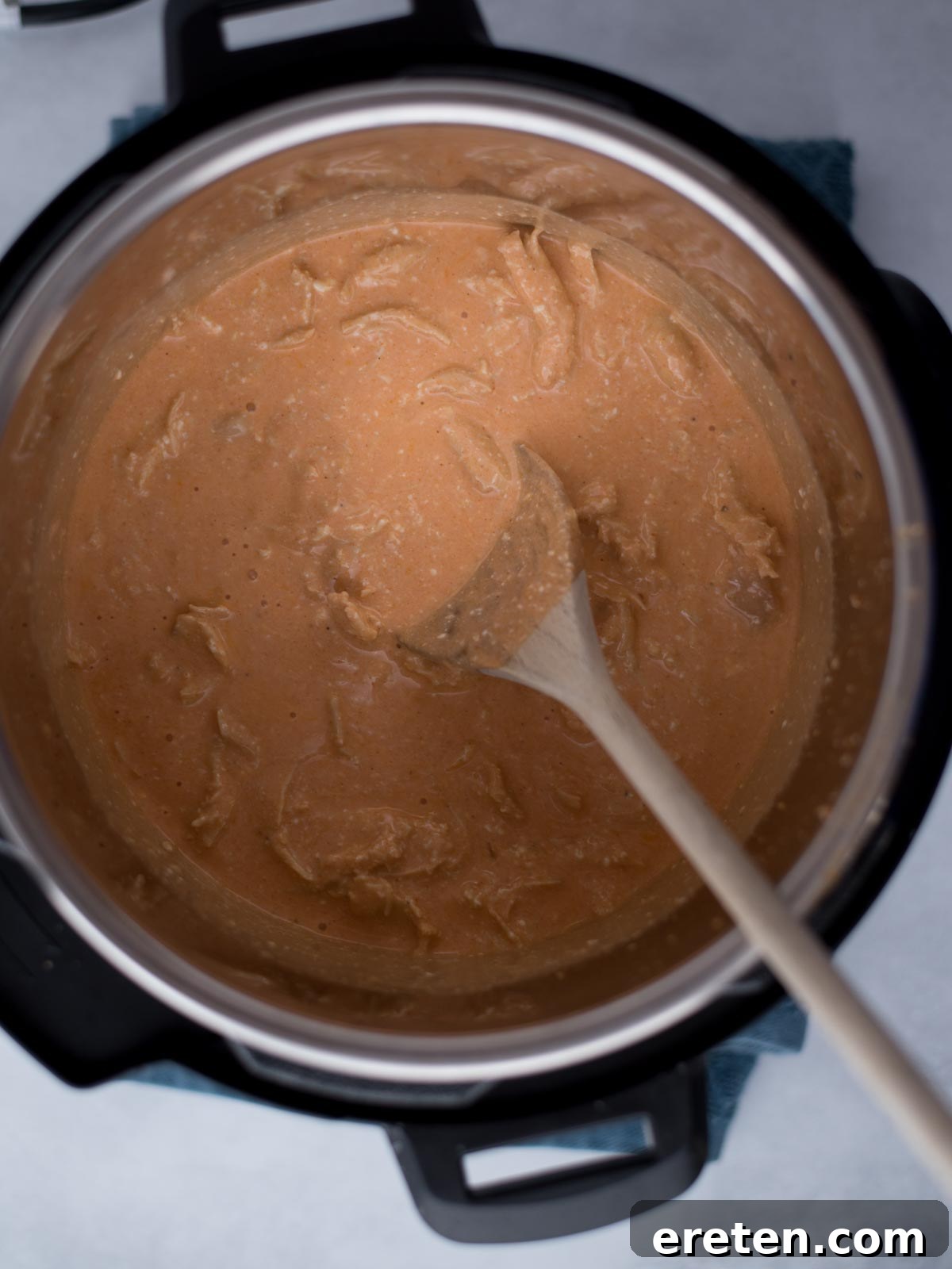 Wooden spoon stirring the creamy buffalo chicken dip inside the instant pot.