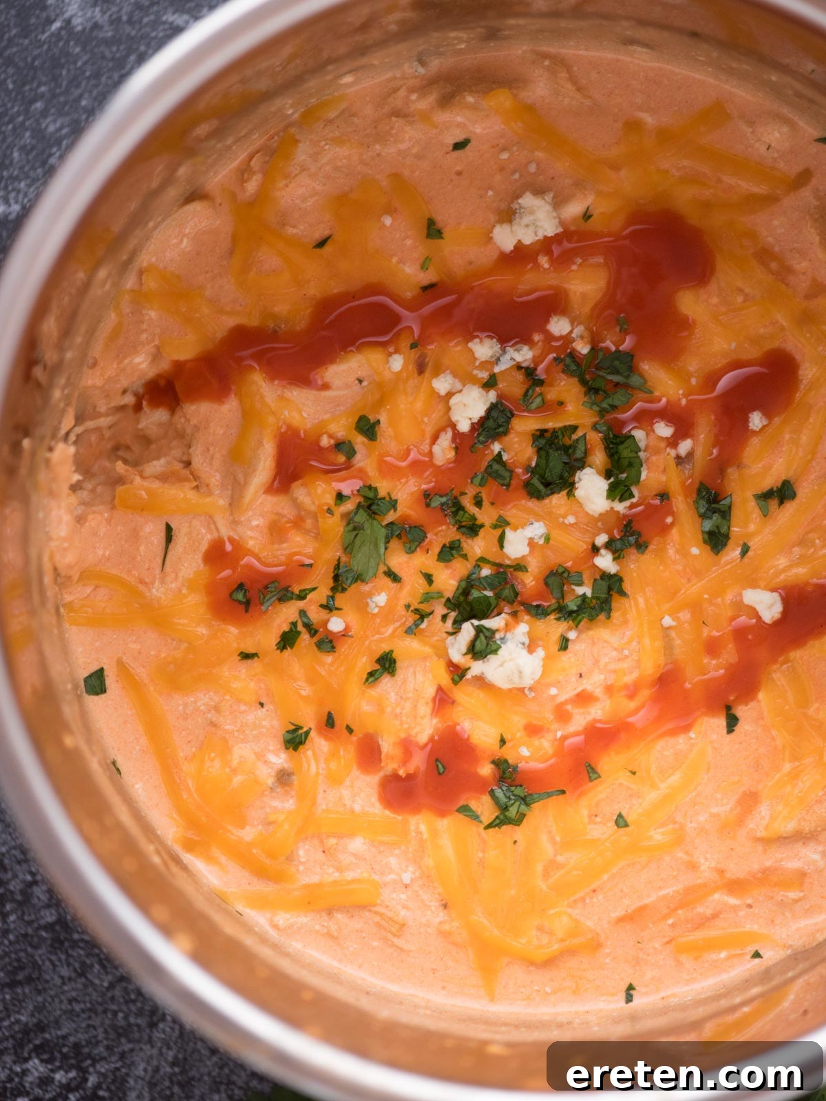 Top view of Buffalo Chicken Dip in a bowl with buffalo sauce drizzled over the top with chopped cilantro and cheese crumbles.